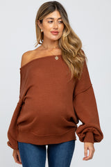 woman wearing a rust oversized off-shoulder maternity sweater and showing her baby bump