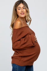woman wearing a rust off-the-shoulder maternity sweater and showing her baby bump