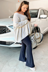 woman wearing a light gray oversized maternity sweater and black flared pants, holding a stylish handbag, with a baby bump visible