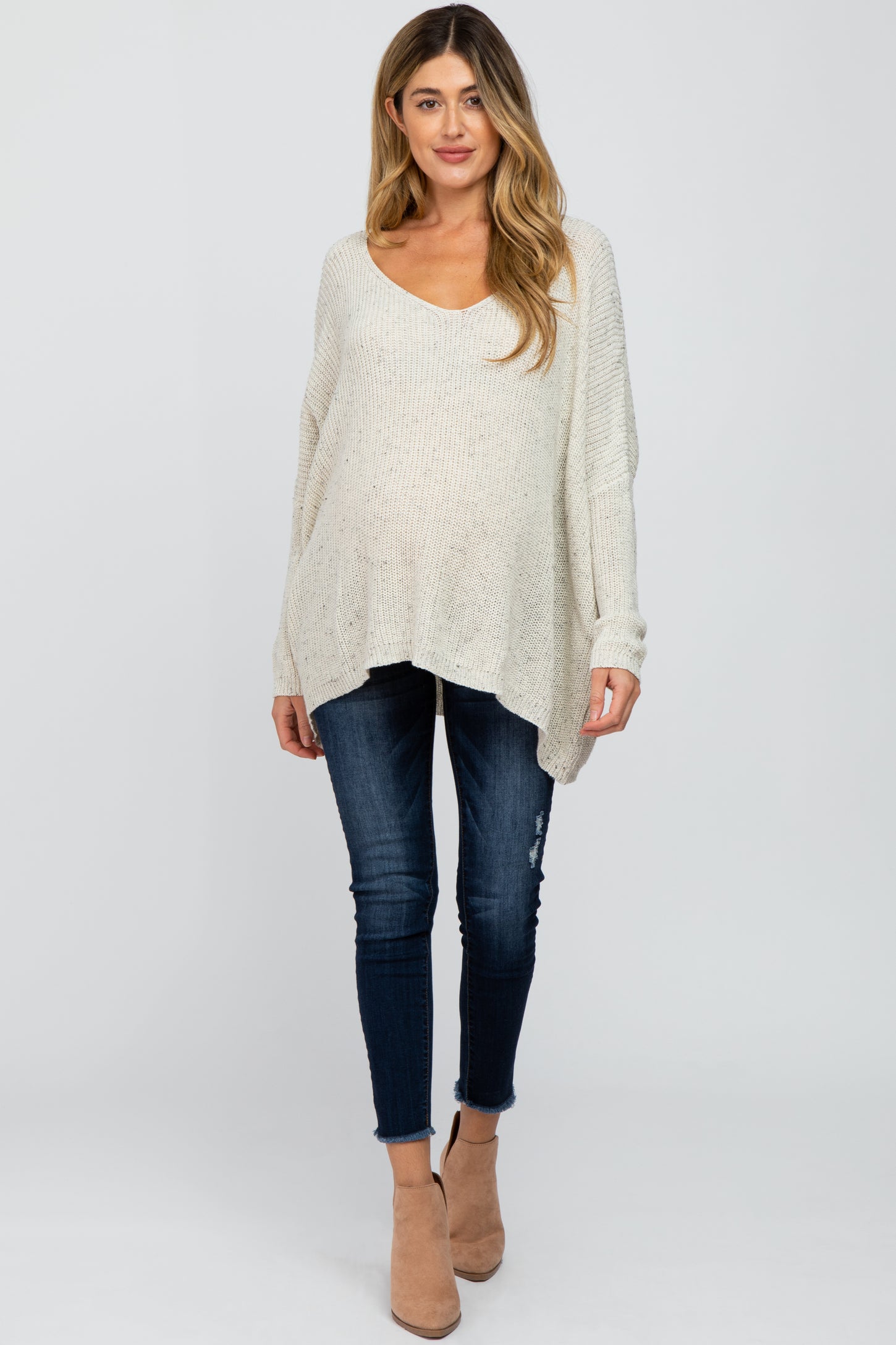 woman wearing a light beige oversized knitted maternity sweater and fitted jeans, with a visible baby bump