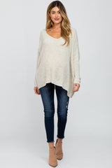 woman wearing a light beige oversized knitted maternity sweater and fitted jeans, with a visible baby bump