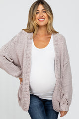 woman wearing a light pink oversized maternity cardigan over a white top and showing her baby bump