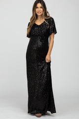 woman wearing a black sequin maternity dress with short flutter sleeves and a tie waist, showing her baby bump