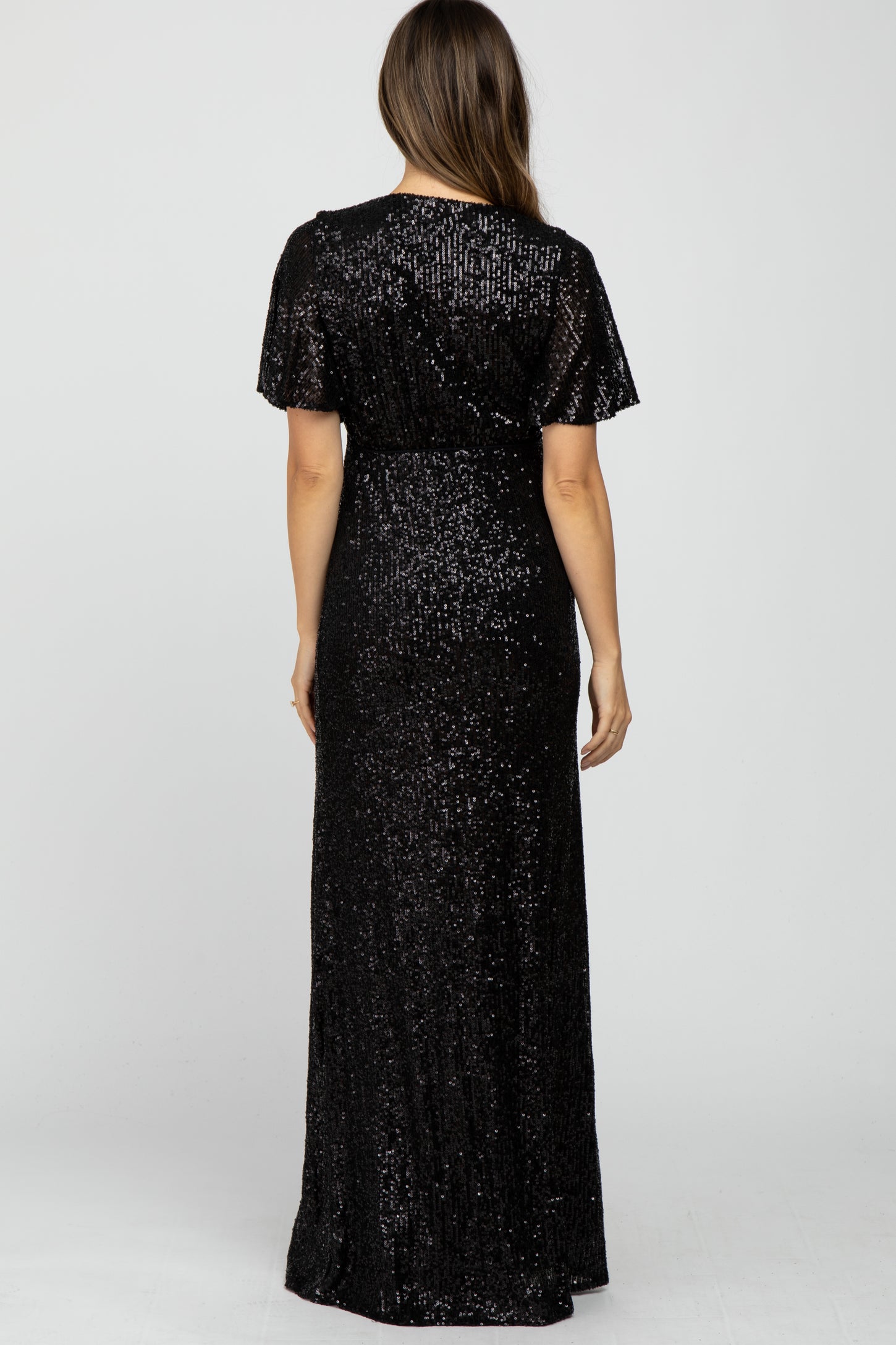 woman wearing a long black sequin maternity dress, showing the back view and a flowing skirt