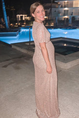 woman wearing a rose gold sequin maternity gown, showcasing her baby bump, standing by a pool at a resort