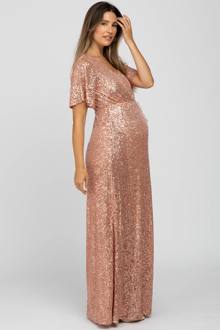 woman wearing a rose gold sequin maternity gown with short sleeves and a stylish wrap design, highlighting her baby bump