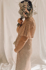 woman wearing a rose gold sequined maternity dress, holding a bouquet of flowers and showing her baby bump