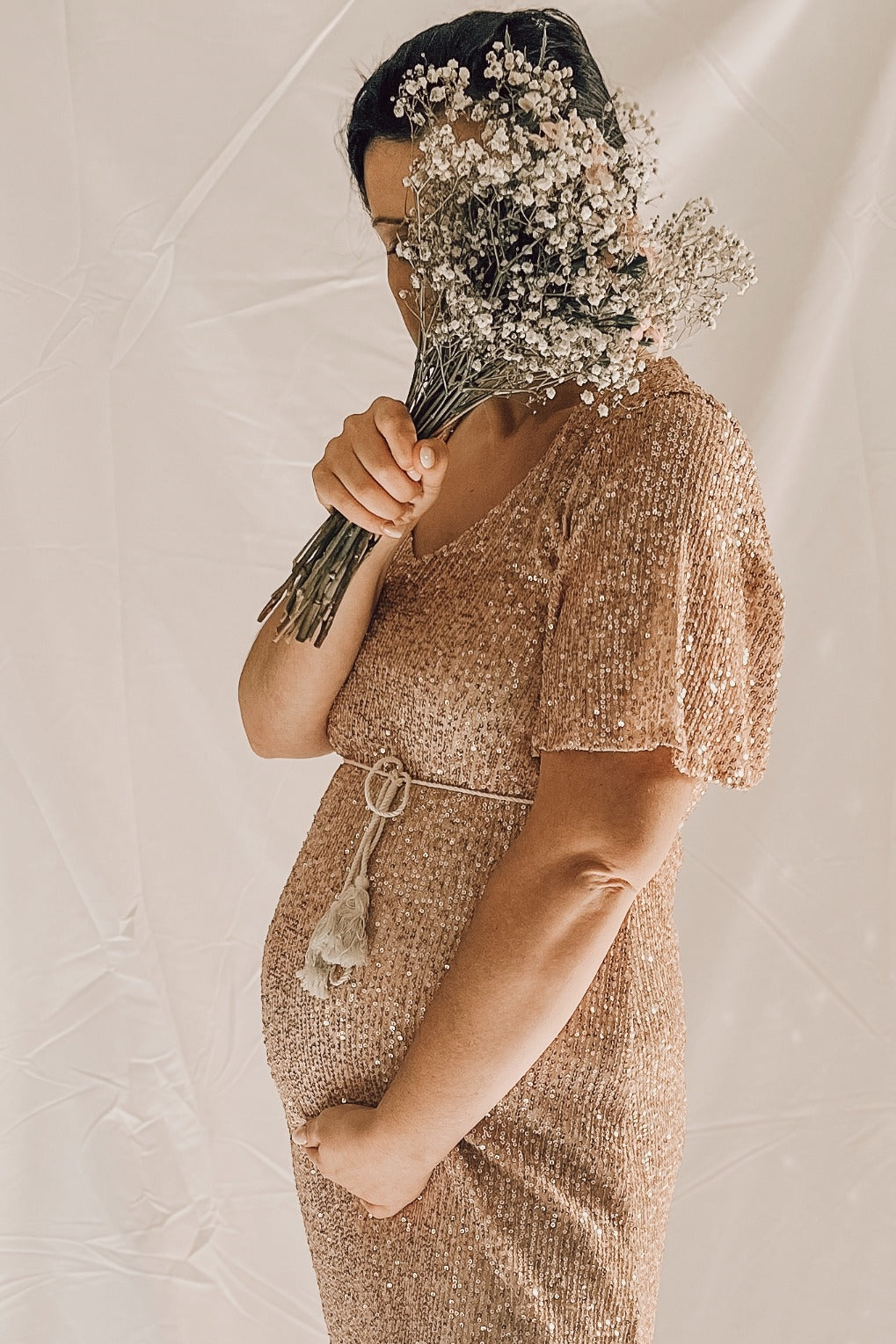 woman wearing a rose gold sequined maternity dress holding a bouquet and showcasing her baby bump