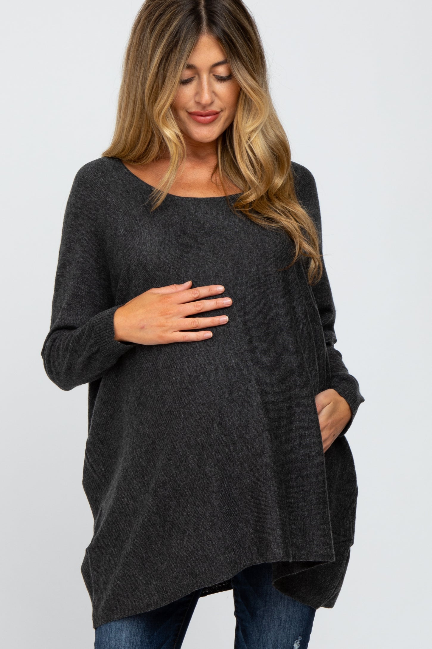 woman wearing a dark gray oversized maternity sweater and cradling her baby bump