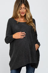 woman wearing a dark gray oversized maternity sweater and cradling her baby bump