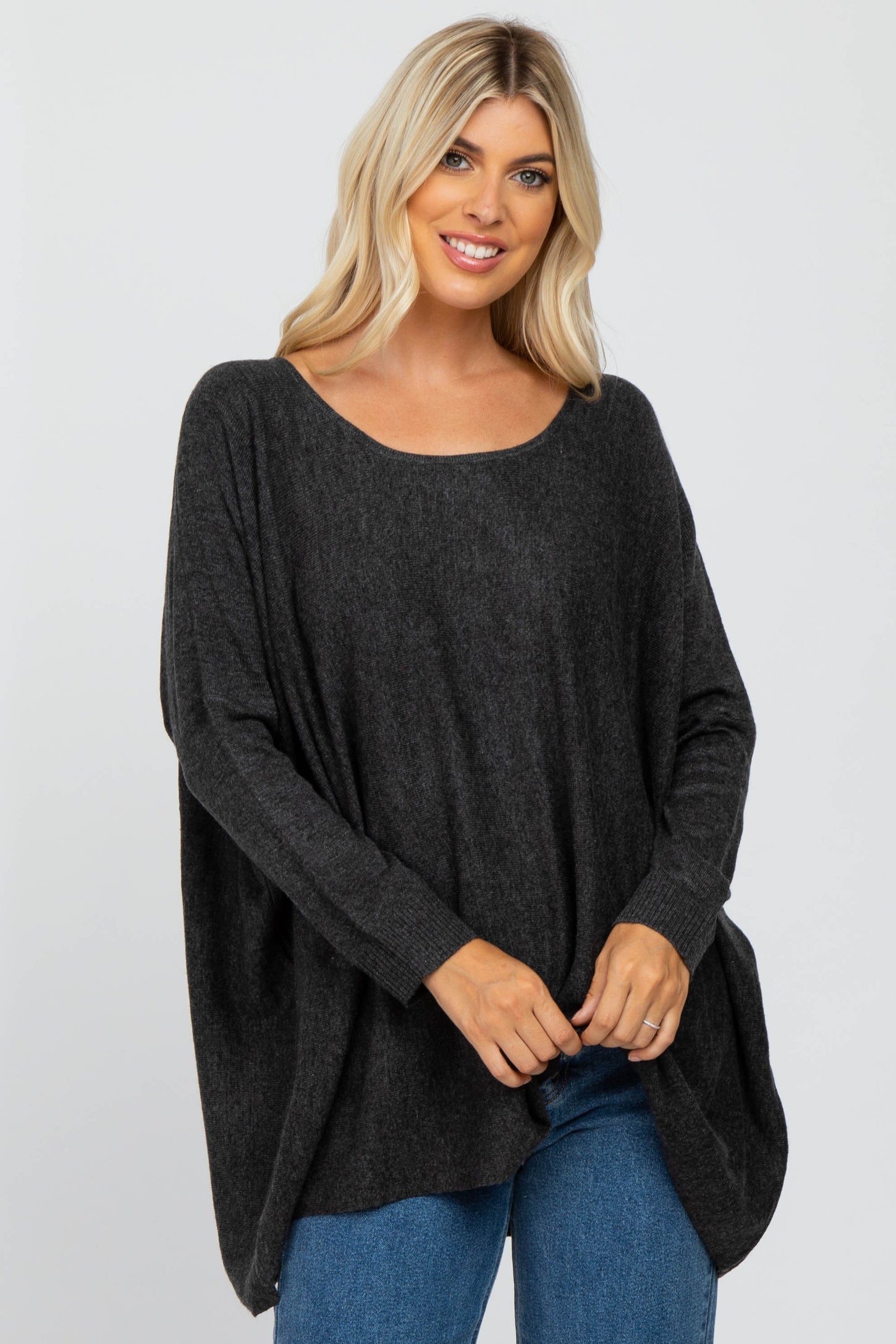 woman wearing a dark gray oversized sweater with a rounded neckline and relaxed fit, paired with blue jeans