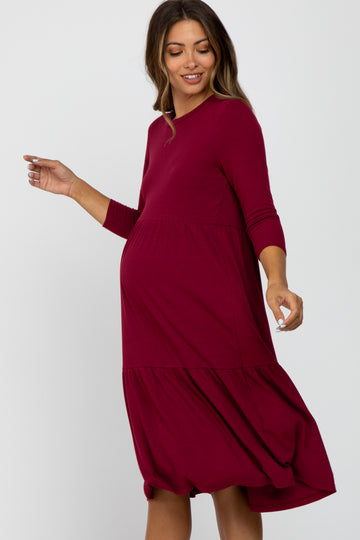 woman wearing a burgundy ribbed maternity dress with a tiered skirt and three-quarter sleeves, showing her baby bump