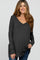 woman wearing a dark gray long sleeve maternity top with a v-neck and gently flowing silhouette, holding her baby bump