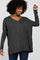 woman wearing a dark gray oversized v-neck top with long sleeves and relaxed fit, smiling with hand raised