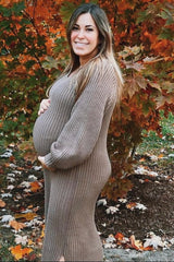 woman wearing a brown ribbed maternity dress and holding her baby bump outdoors with autumn leaves in the background