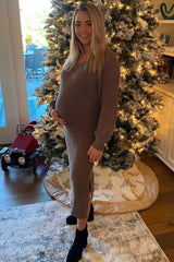 woman wearing a brown ribbed maternity dress with long sleeves and a baby bump, standing next to a decorated Christmas tree
