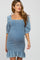 woman wearing a blue denim smocked maternity dress with puff sleeves and ruffle hem, showing her baby bump