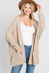 woman wearing a beige open knit cardigan with pockets over a white tank top and jeans, smiling and wearing a hat