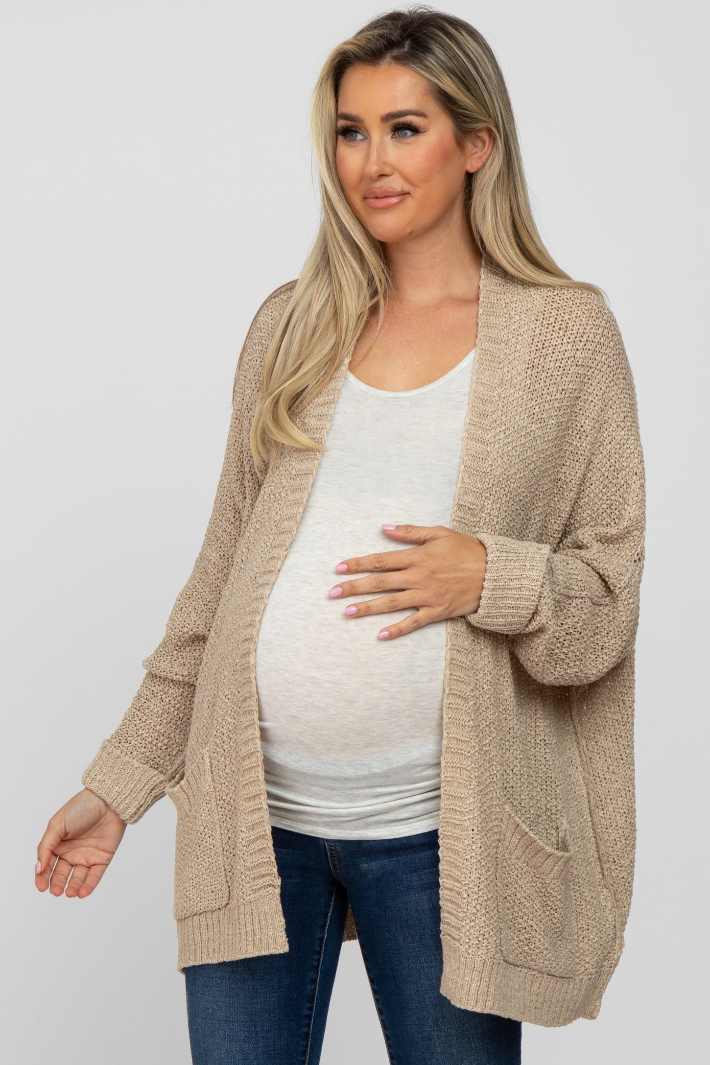 woman wearing a beige open-knit maternity cardigan and a light gray top, with her baby bump visible