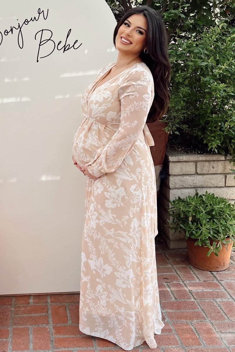woman wearing a beige floral maternity maxi dress and holding her baby bump