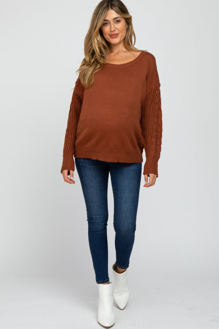 woman wearing a rust cable knit sleeve maternity sweater and blue skinny jeans, with a visible baby bump