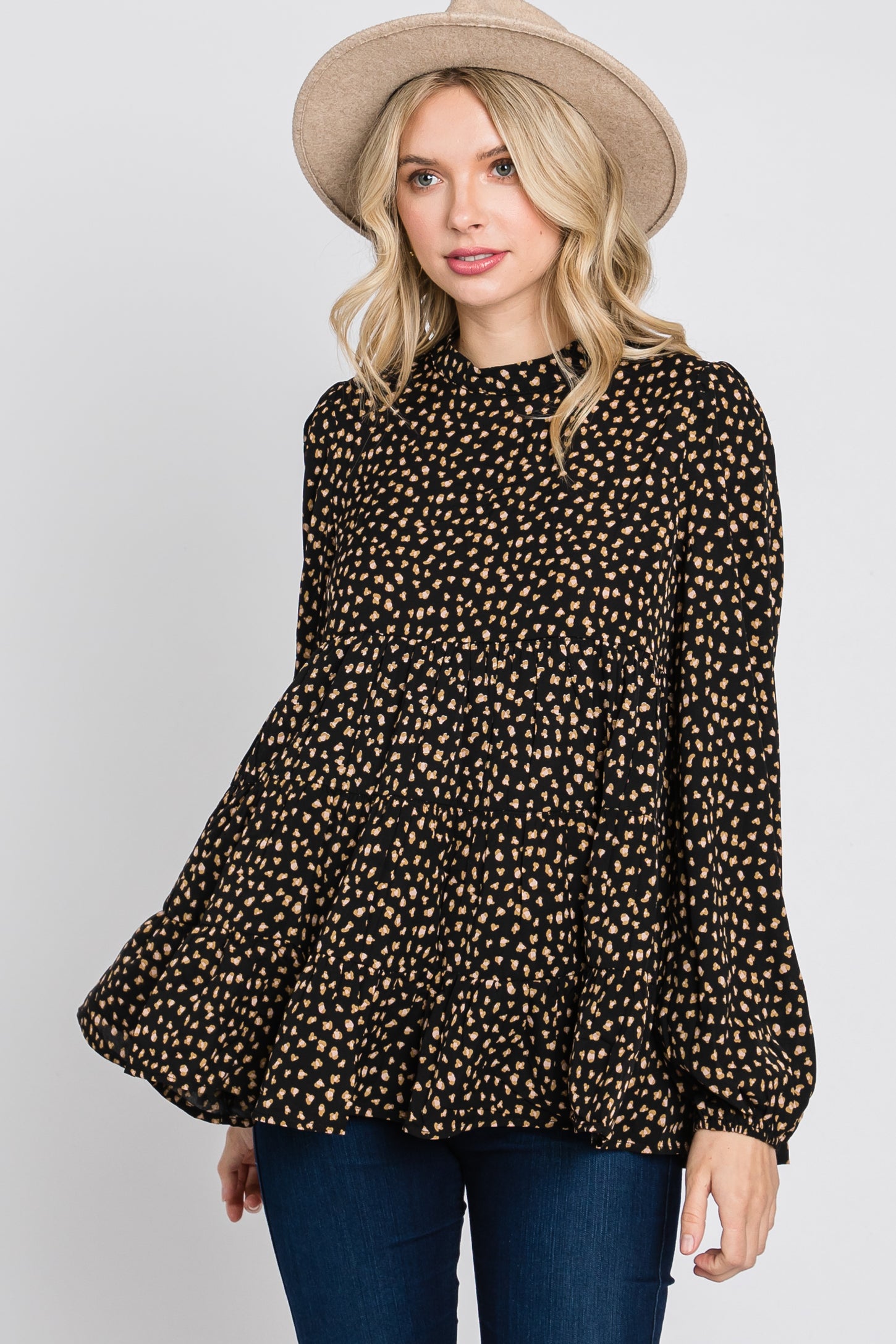 woman wearing a black and tan polka dot peplum blouse with long sleeves and a high neckline, styled with a hat