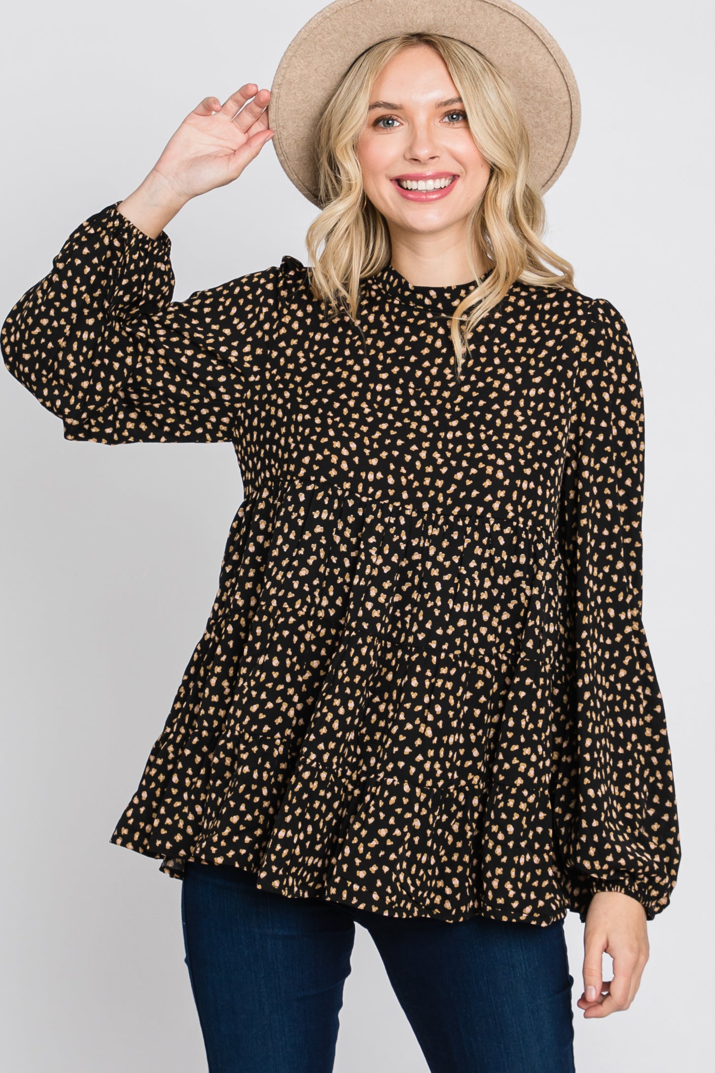 woman wearing a black and gold polka dot long sleeve peplum top with a high neckline and a wide-brimmed hat