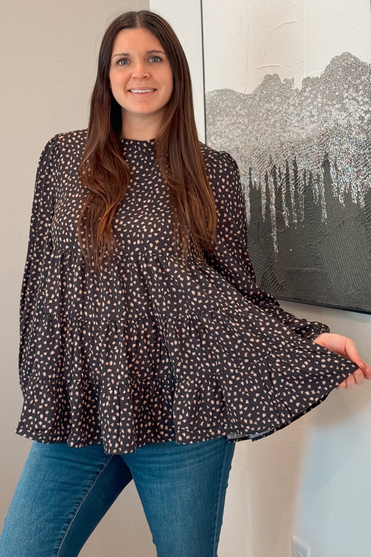 woman wearing a black and white polka dot tiered blouse with long sleeves and blue jeans