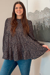 woman wearing a black and white polka dot tiered blouse with long sleeves and blue jeans