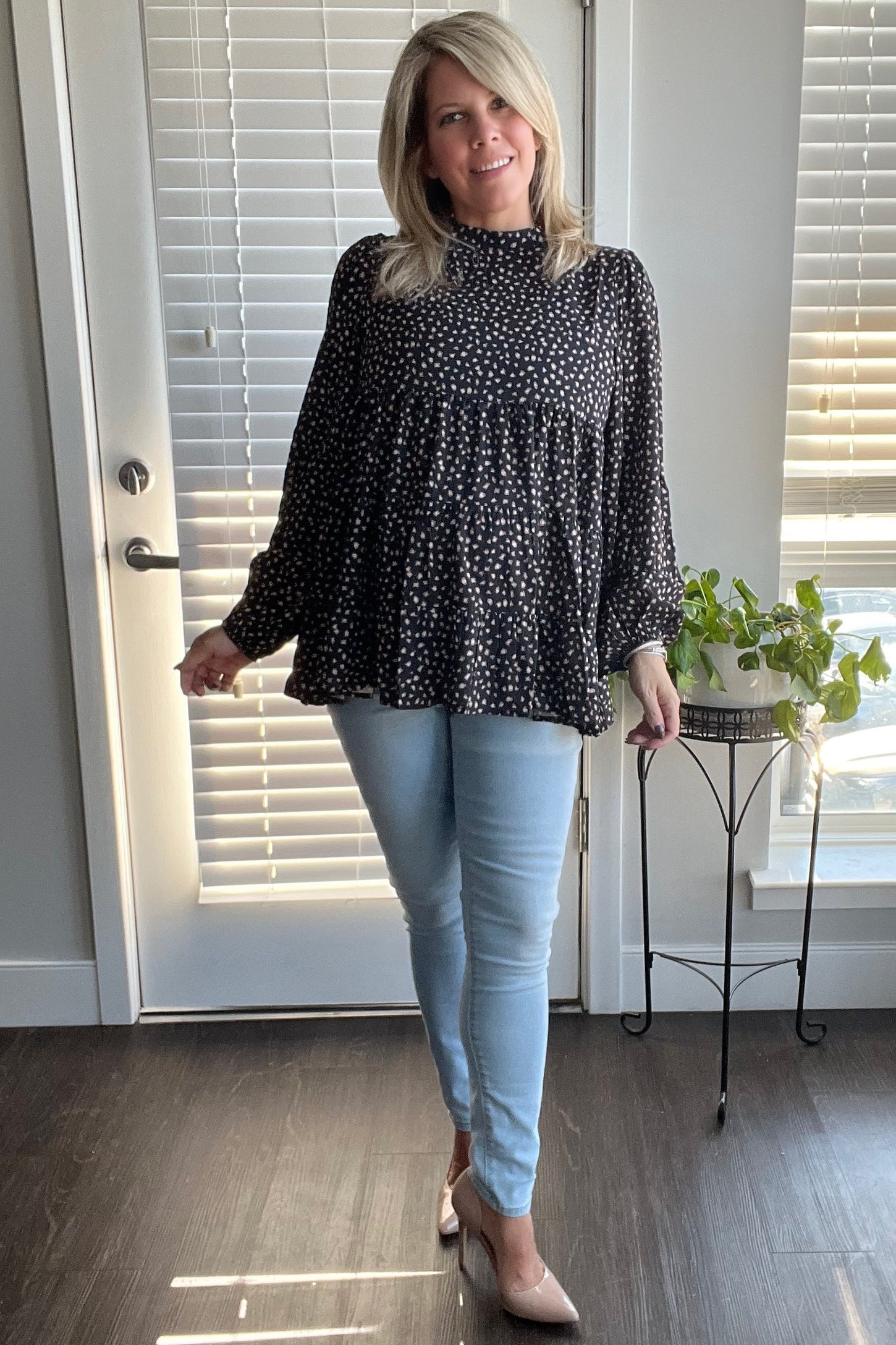 woman wearing a black and white polka dot peplum top with long sleeves and light blue skinny jeans
