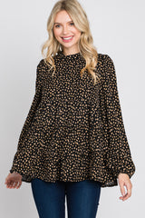 woman wearing a black blouse with tan polka dots and bell sleeves, smiling and posing against a plain background