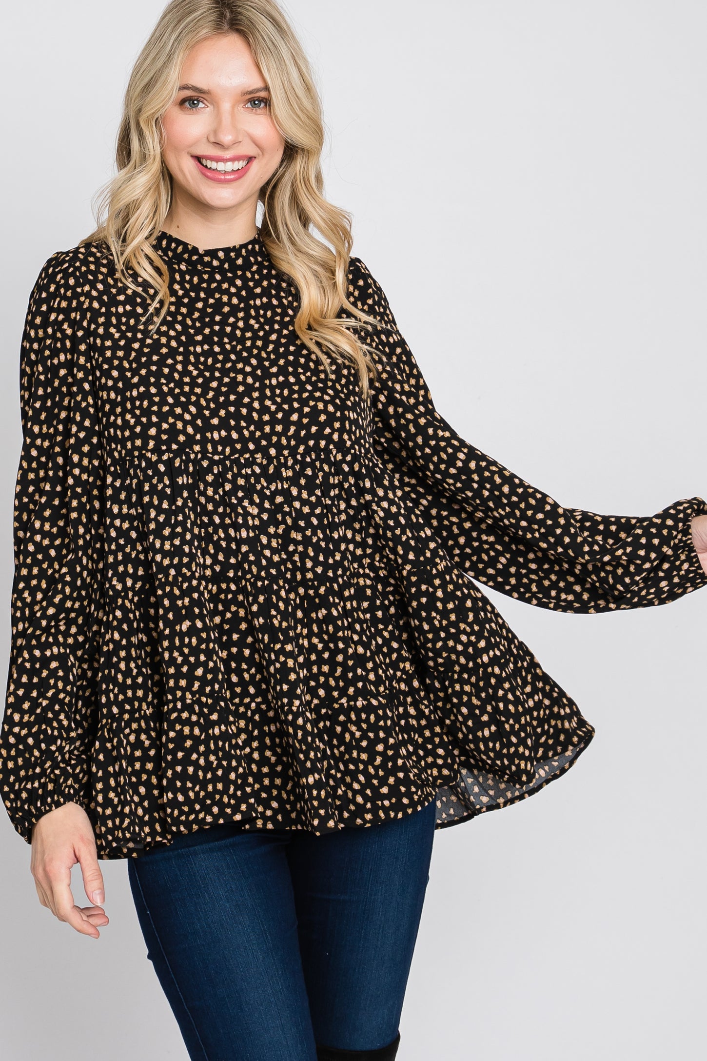 woman wearing a black long sleeve top with a cream polka dot pattern and a loose, tiered design, smiling at the camera