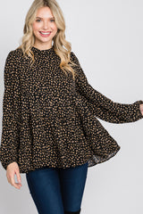 woman wearing a black long sleeve top with a cream polka dot pattern and a loose, tiered design, smiling at the camera