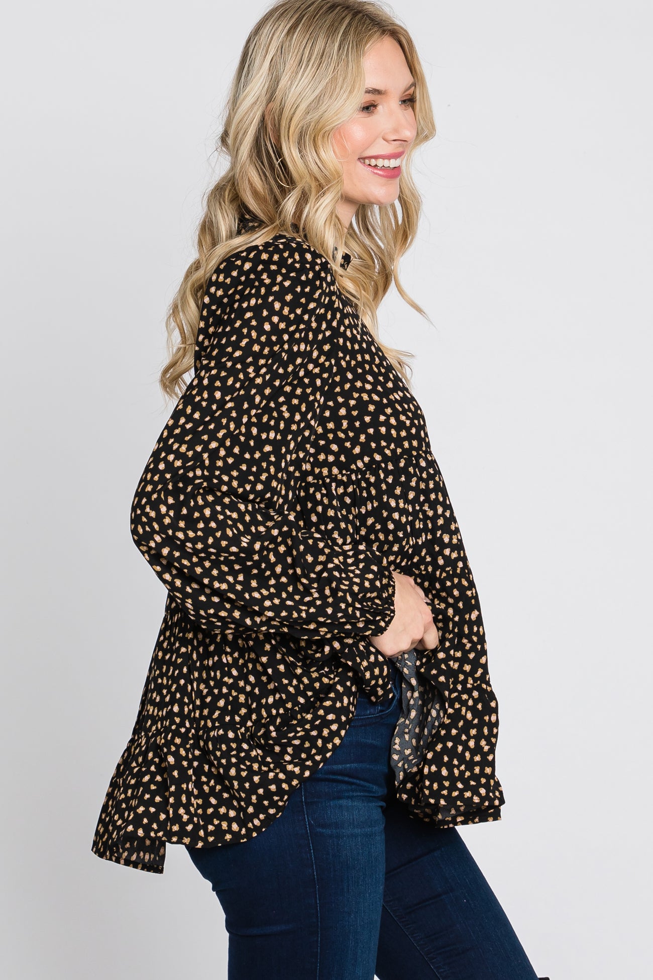 woman wearing a black and tan polka dot blouse with long sleeves and a ruffled hem, paired with blue jeans
