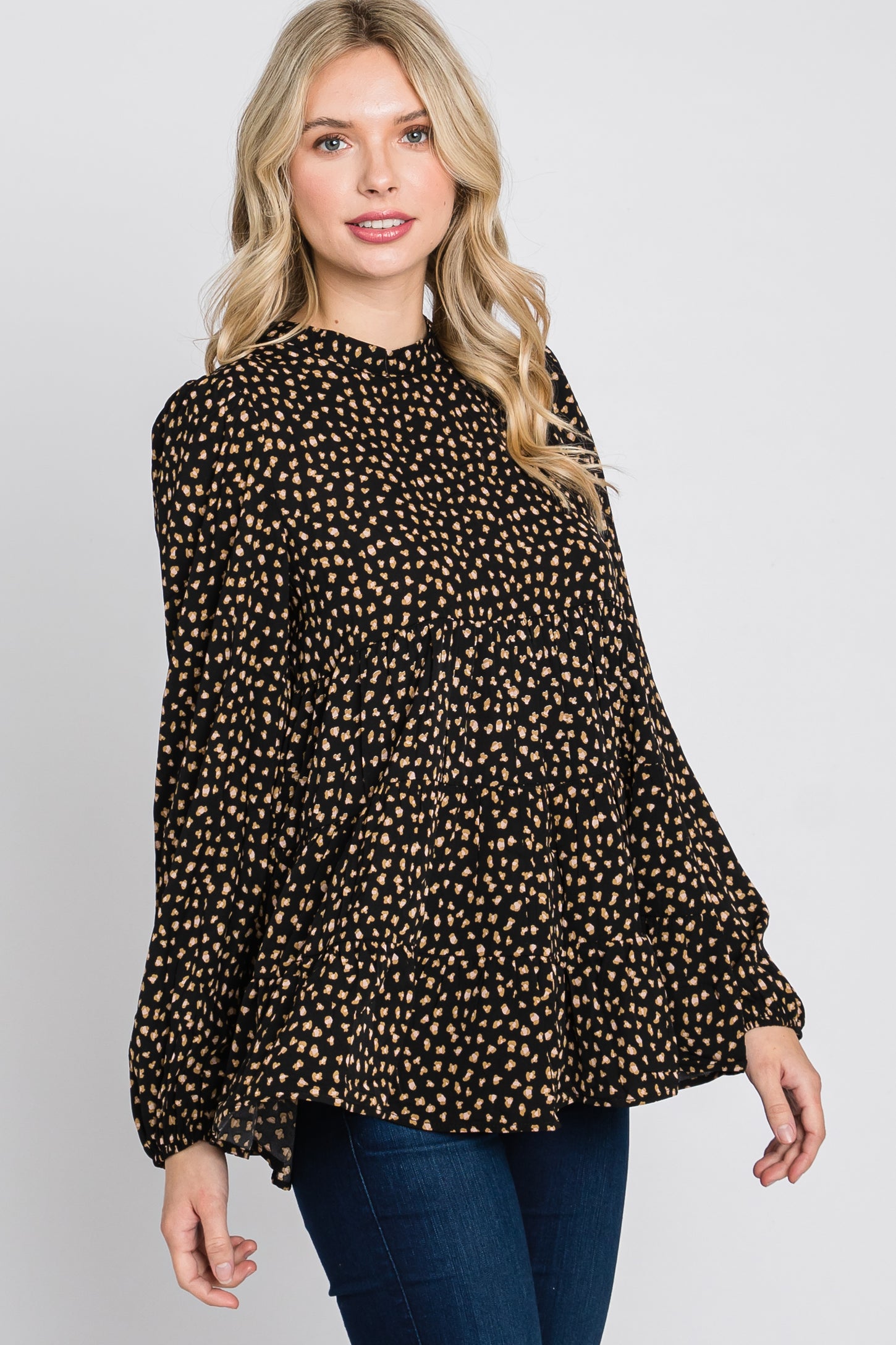 woman wearing a black long sleeve top with a gold polka dot pattern and a pleated design, paired with dark jeans