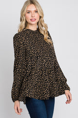 woman wearing a black long sleeve top with a gold polka dot pattern and a pleated design, paired with dark jeans