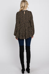 woman wearing a black and gold spotted peplum top with long bell sleeves and back keyhole detail, paired with skinny jeans and over-the-knee boots