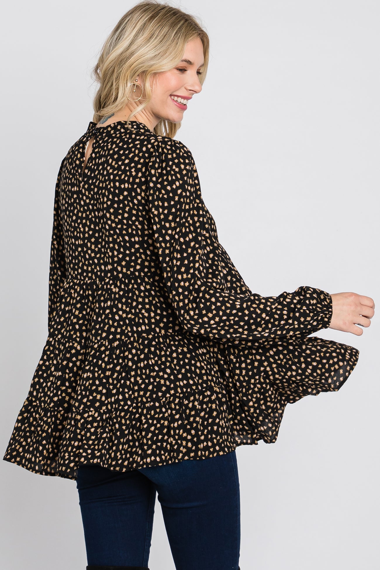 woman wearing a black peplum top with beige polka dots and a back keyhole detail, smiling while turning to the side