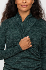 woman wearing a dark green wrap-style long sleeve top with textured fabric and a cozy neckline