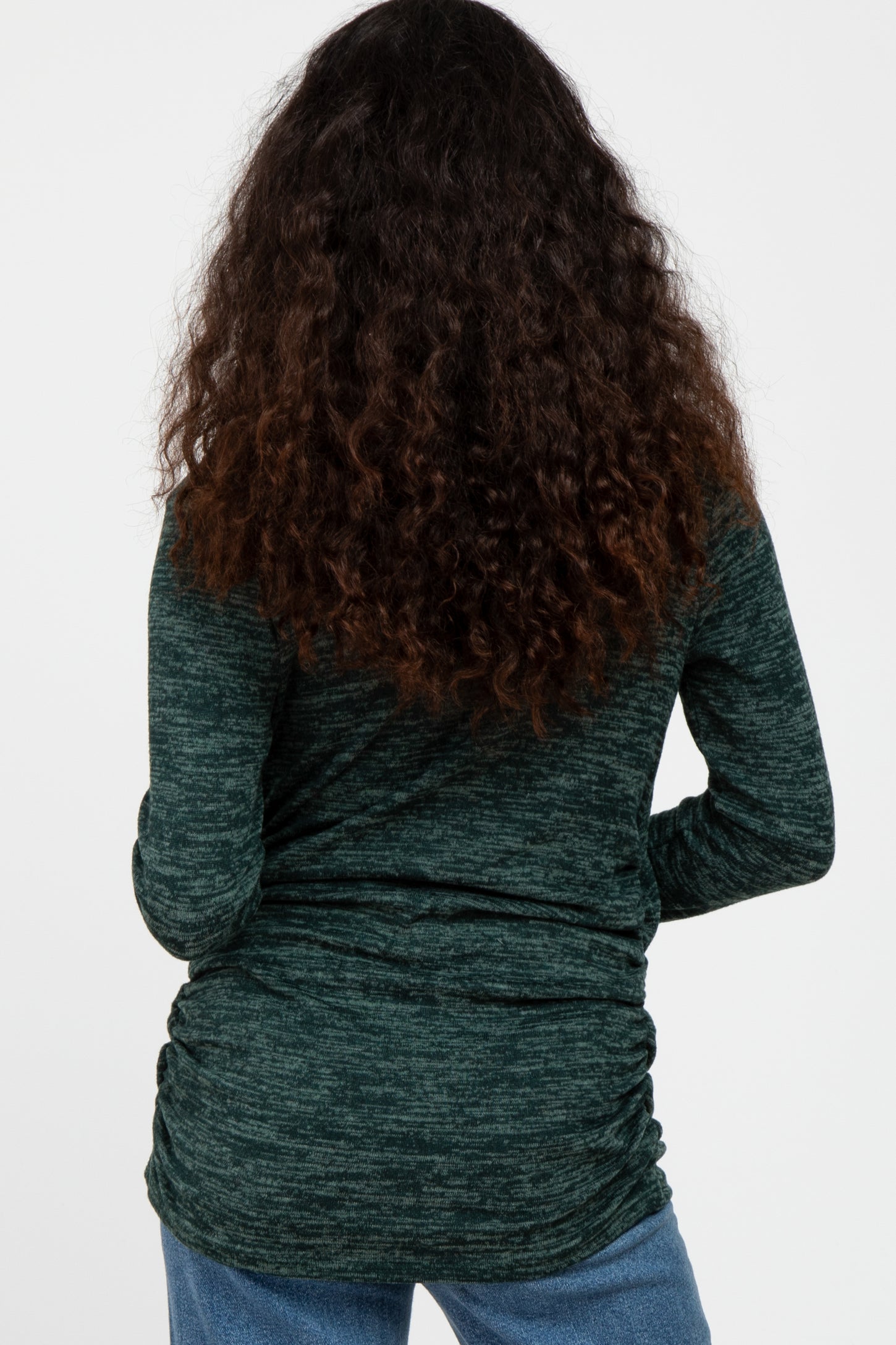 woman wearing a dark green long sleeve top with gathered detailing at the sides, seen from the back