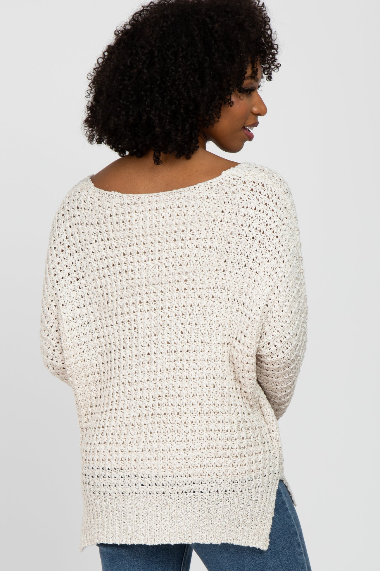 woman wearing a light beige open knit sweater with a loose fit and side slits, paired with blue jeans