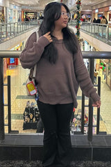 woman wearing a brown oversized sweater and black flared pants standing in a shopping mall