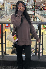 woman wearing a brown oversized sweater with black flared pants and holding a bag, smiling in a shopping mall