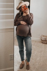 woman wearing a brown oversized maternity sweater and light blue jeans, holding her baby bump in front of a mirror