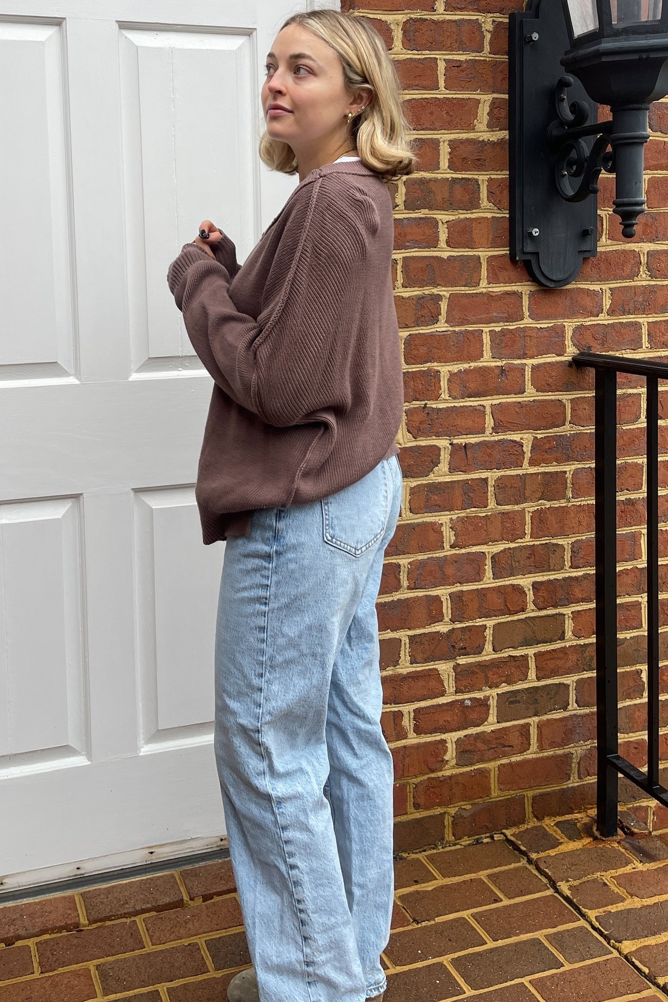 woman wearing a brown oversized sweater and light blue high-waisted jeans, standing outside near a brick wall