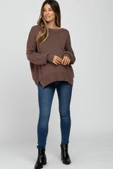 woman wearing a brown oversized maternity sweater with a relaxed fit and blue skinny jeans