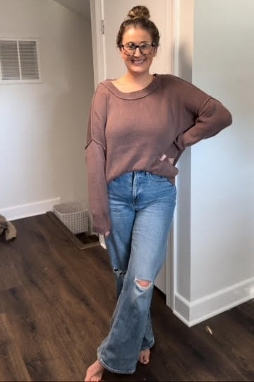 woman wearing a mauve oversized sweater and light blue ripped flared jeans, standing with one hand on her hip