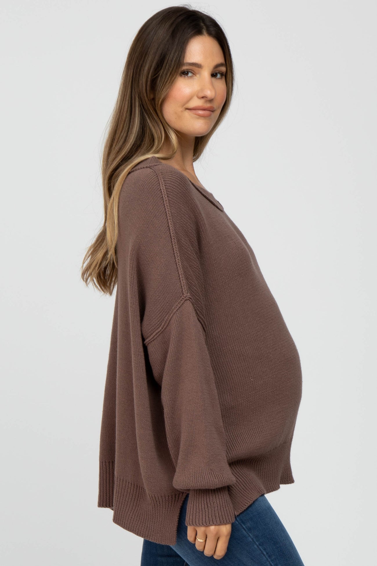 woman wearing a brown oversized maternity sweater and showing her baby bump