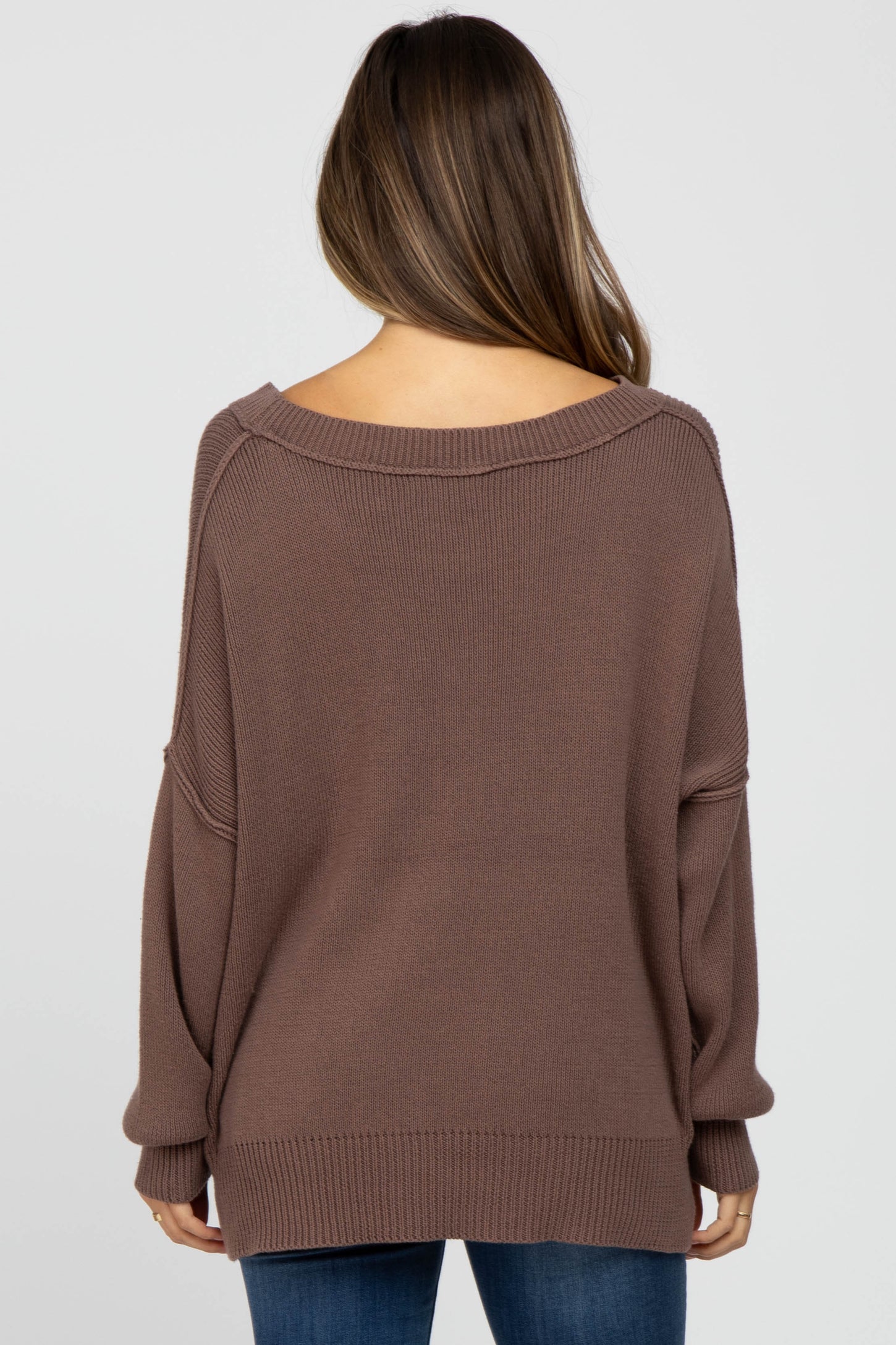 woman wearing a soft brown oversized maternity sweater, seen from the back, styled with relaxed fit and dropped shoulder seams