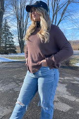 Woman in brown oversized sweater and distressed blue jeans posing outdoors in winter